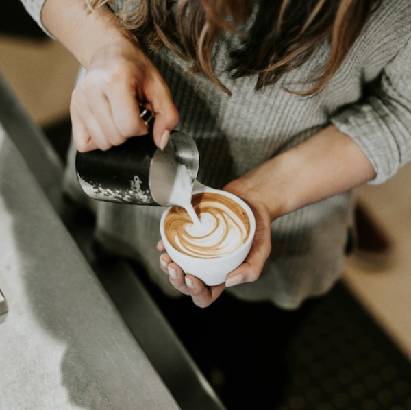 An over-head shot of someone making a latte with frothed milk from a jug